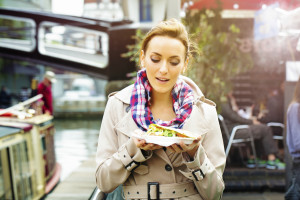 Young British woman looks at take-out food with appetite as she walks out in London, UK on a late Autumn afternoon.  She is dressed in warm clothing and a warm light bathes the image.